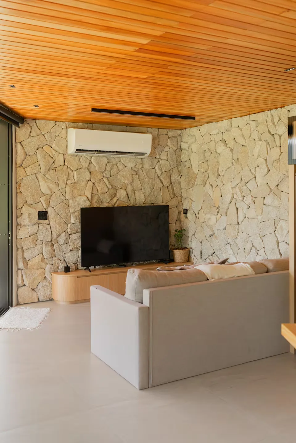 Sala com sofá e TV na parede de pedra